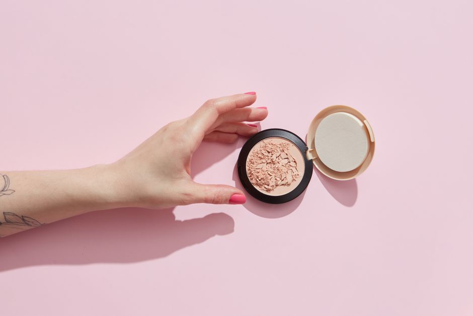 Stylish image of a hand reaching for open face powder on a soft pink background.