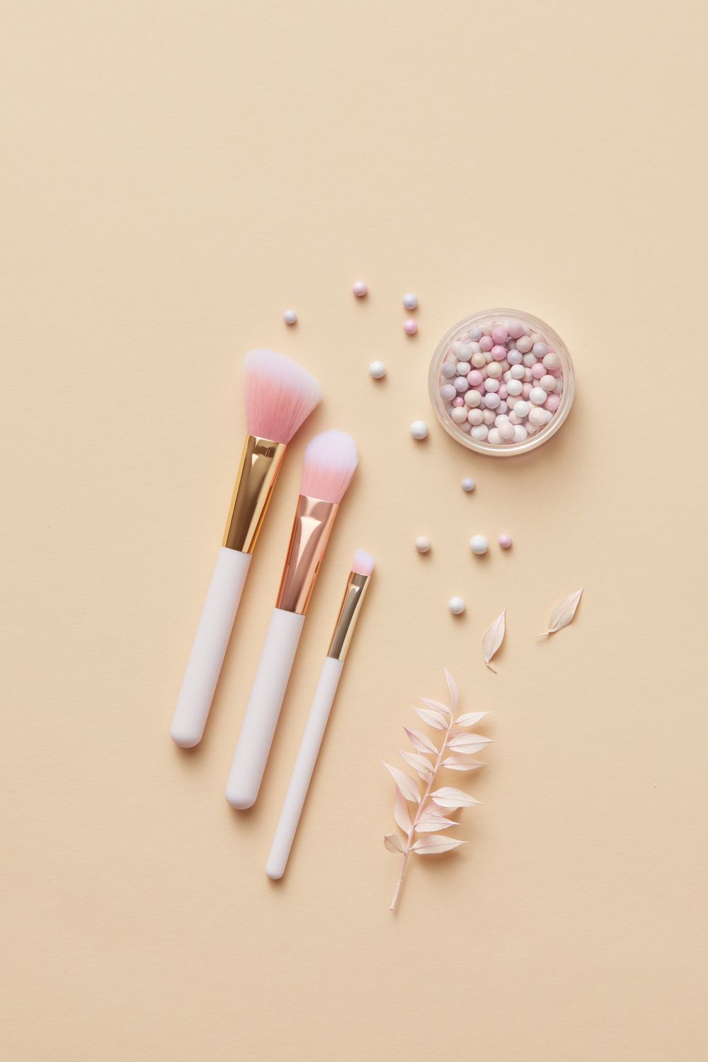 Makeup brushes and pearls on a beige backdrop