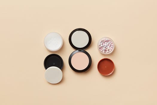 Flat lay of assorted makeup containers and powder balls on a beige surface, showcasing beauty essentials.