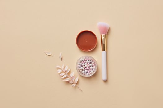Elegant flat lay of a makeup brush, container with powder balls, and dried leaves on yellow pastel surface.