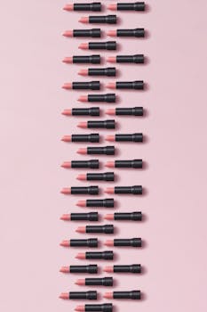 Stylish vertical arrangement of pink lipsticks on a pastel pink surface, perfect for beauty themes.