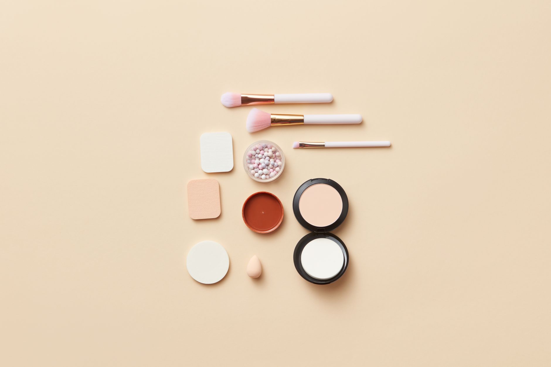 A flat lay of makeup brushes and cosmetics on a beige background, perfect for beauty themes.