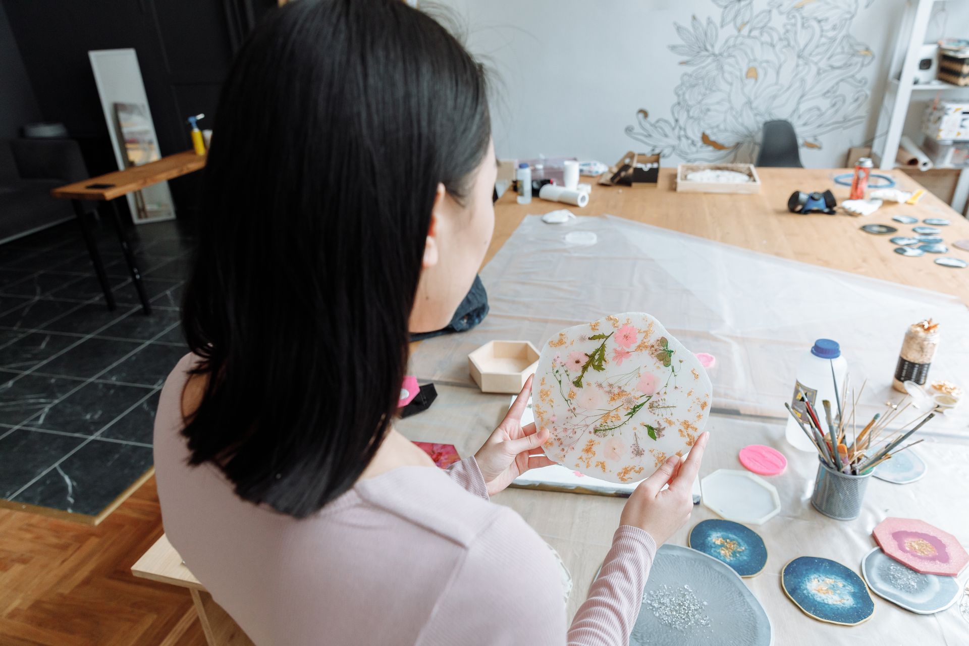 A woman artist crafting a decorative resin piece in a modern studio setting with various art materials.