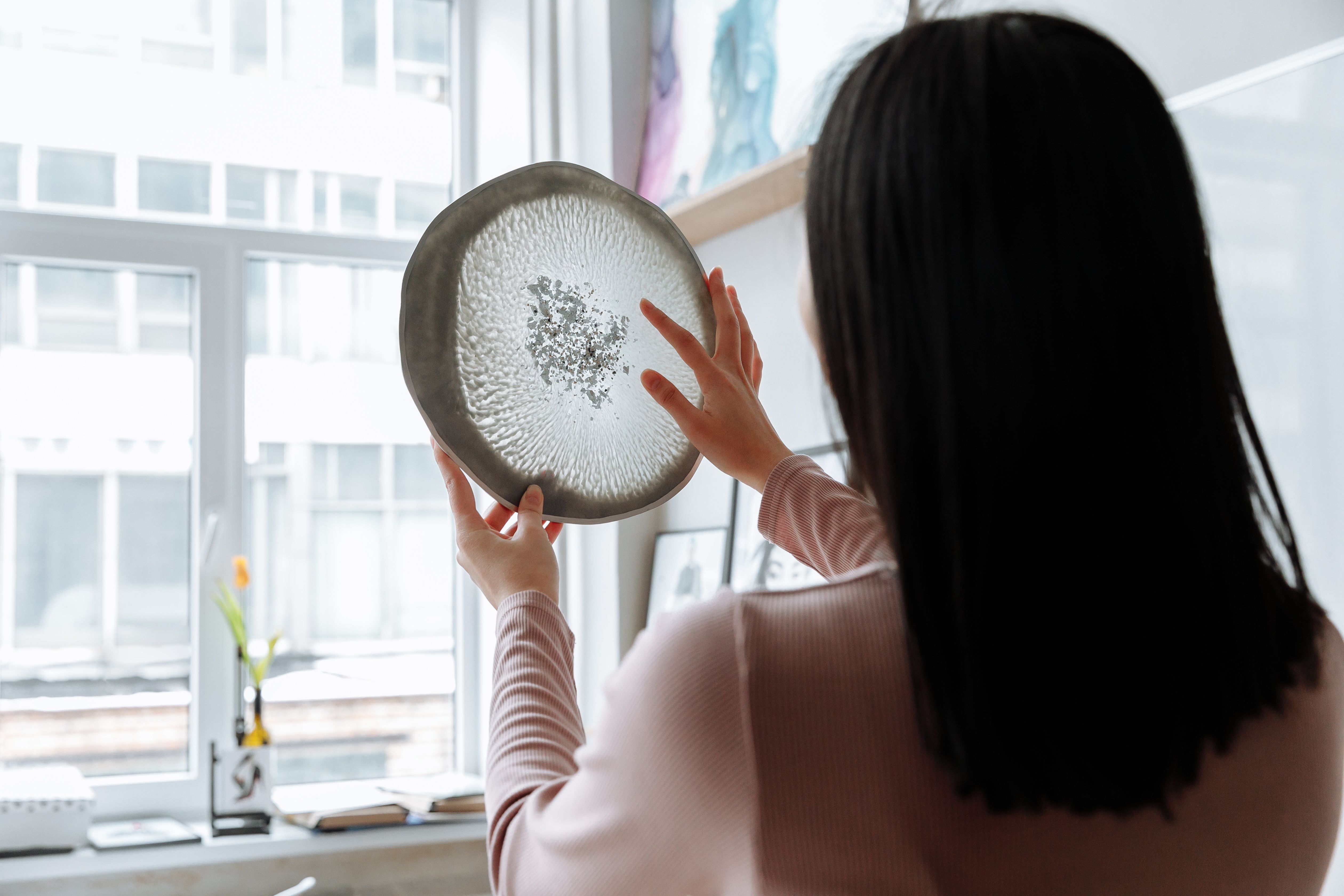 A woman with long hair holds an artistic resin plate by a window, creating a modern art vibe.