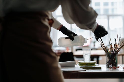 Hands in Gloves Pouring Water from Bottle to Glass