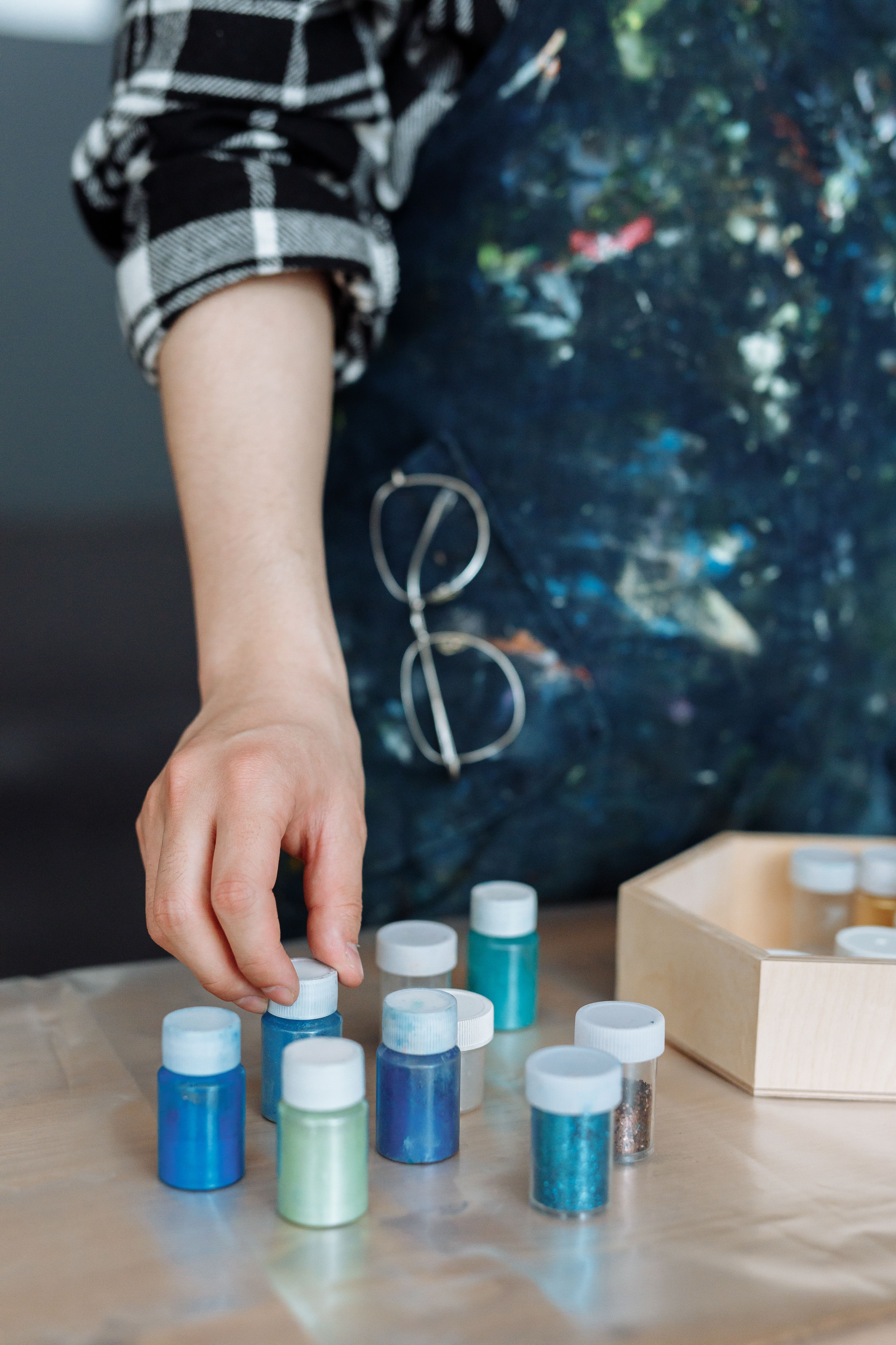 hand arranging small glitter jars in blue and teal shades on a craft table