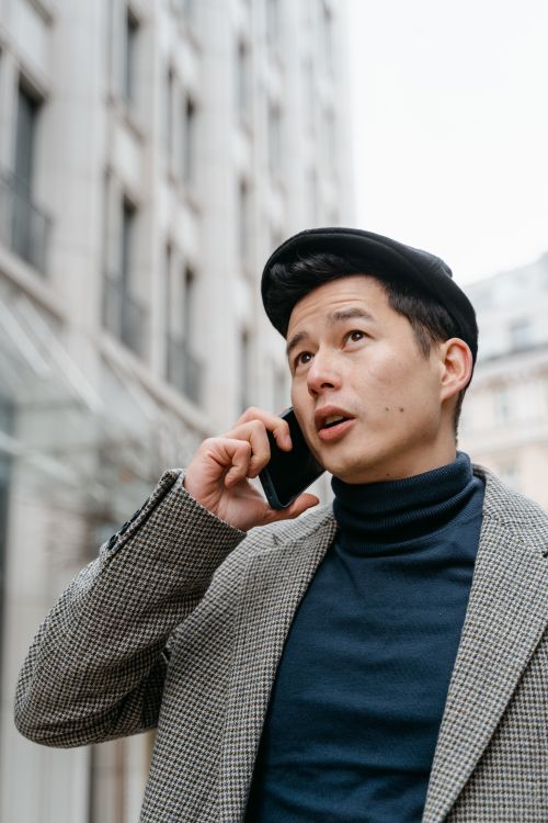 Free Stylish man in a city talking on a smartphone outdoors, wearing a coat and hat. Stock Photo