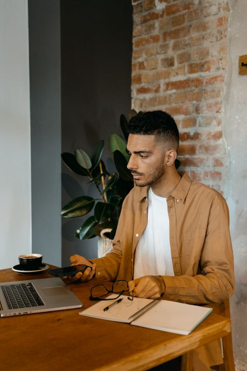 Free Focused man using laptop and smartphone at a wooden table indoors. Stock Photo