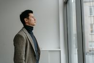 Man in Gray and Black Checkered Dress Shirt Standing Beside White Wall