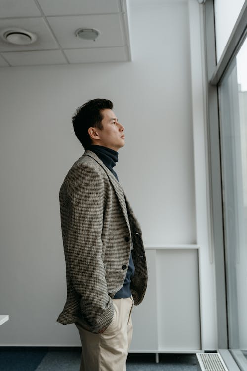Free Man in Gray Sweater Standing Beside White Wall Stock Photo