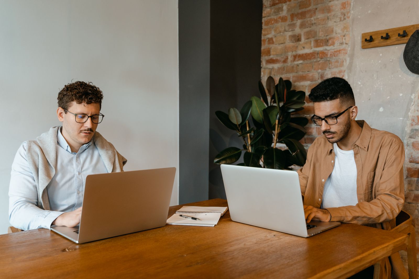 Two colleagues working side by side on laptops at a shared wooden table — photo by MART PRODUCTION on Pexels