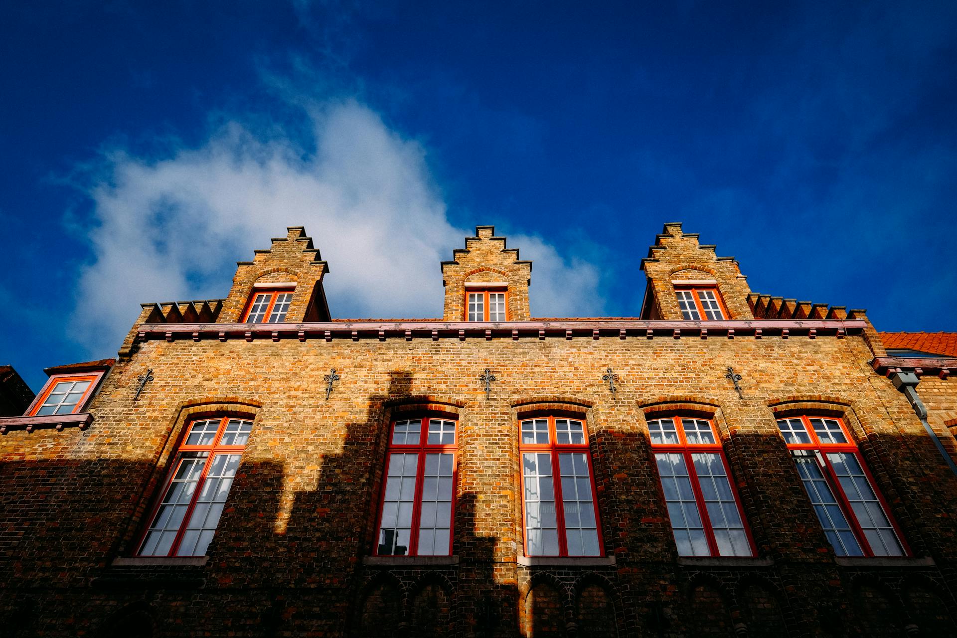 Low angle view of a historic brick building with gable roofs under a bright blue sky.