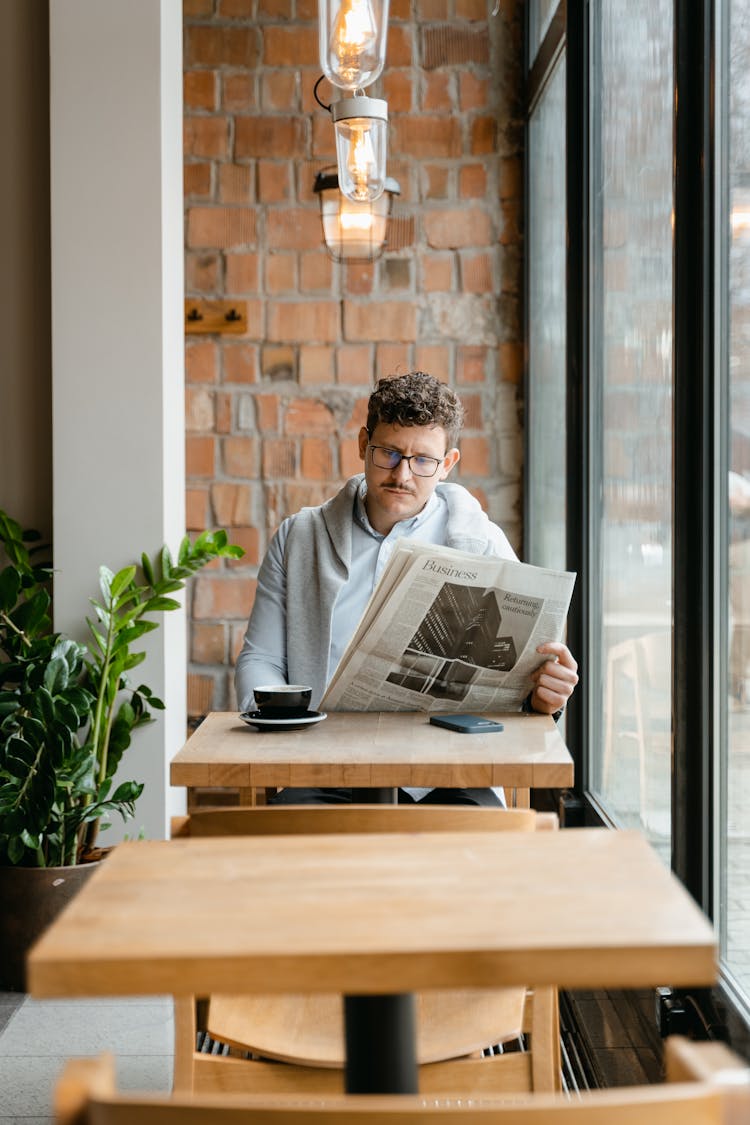 A Man Reading A Newspaper At A Coffee Shop