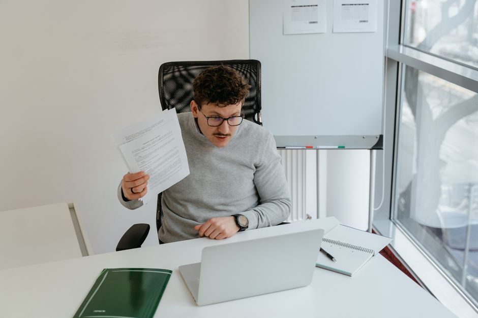 Caucasian man wearing glasses working at a laptop in a modern office setting with documents. Caucasian man wearing glasses working at a laptop in a modern office setting with documents.