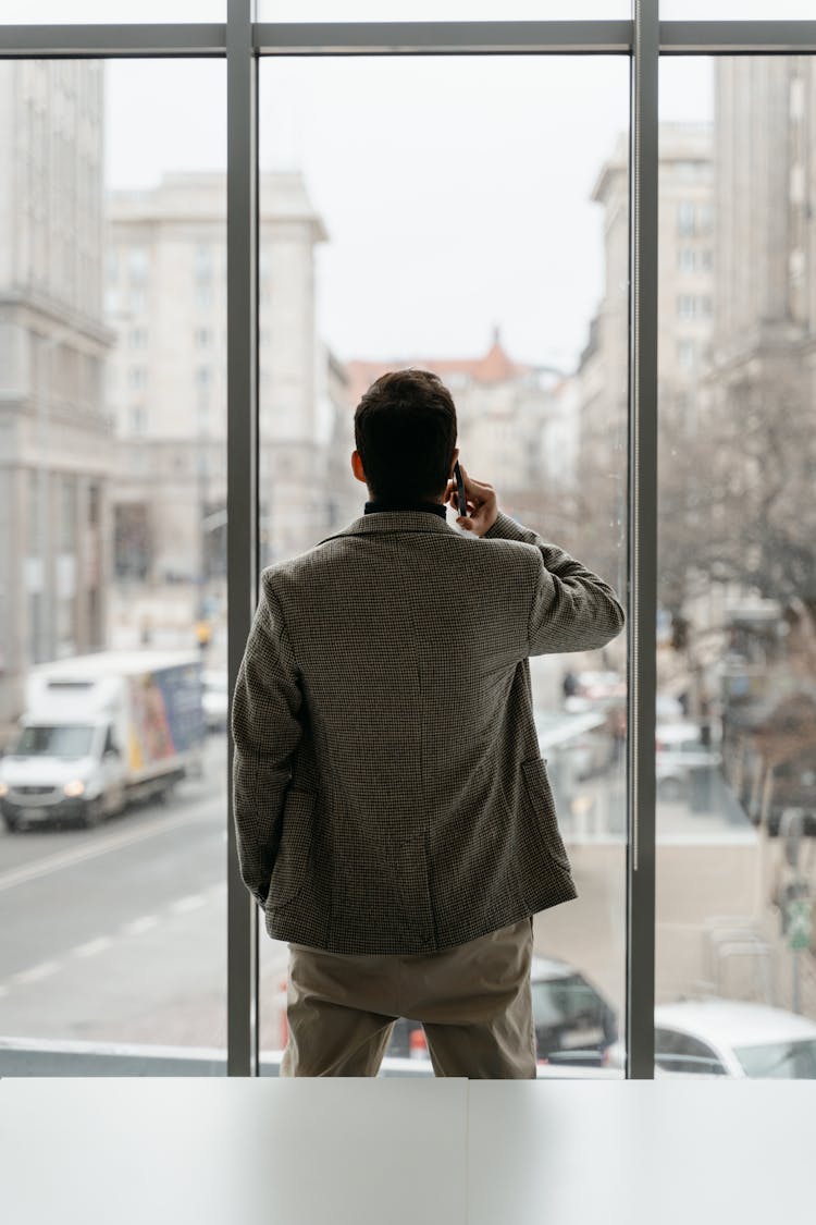 Back View Of A Man In Gray Blazer Taking A Phone Call While Standing In Front Of Glass Window