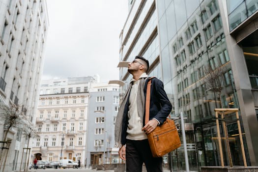 Man exploring city streets with a leather sling bag, looking at modern architecture.