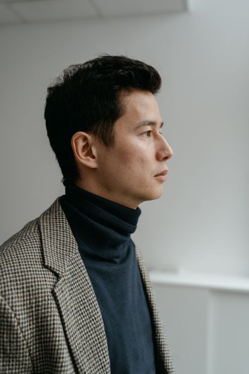 Free Side profile of a man wearing a checkered coat and navy turtleneck against a simple background. Stock Photo