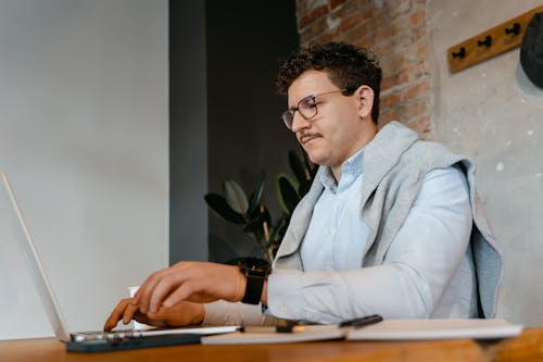 Low-Angle Shot of a Man Wearing Eyeglasses while Using a Laptop