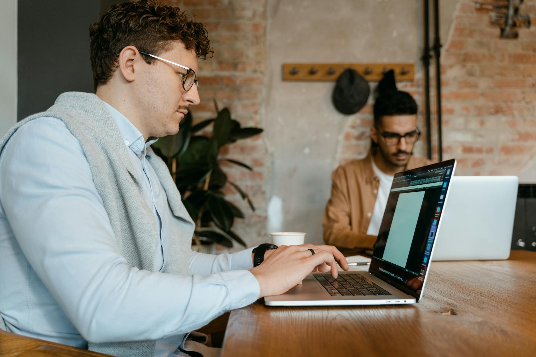 Two young men working on laptops in a stylish modern office setting.