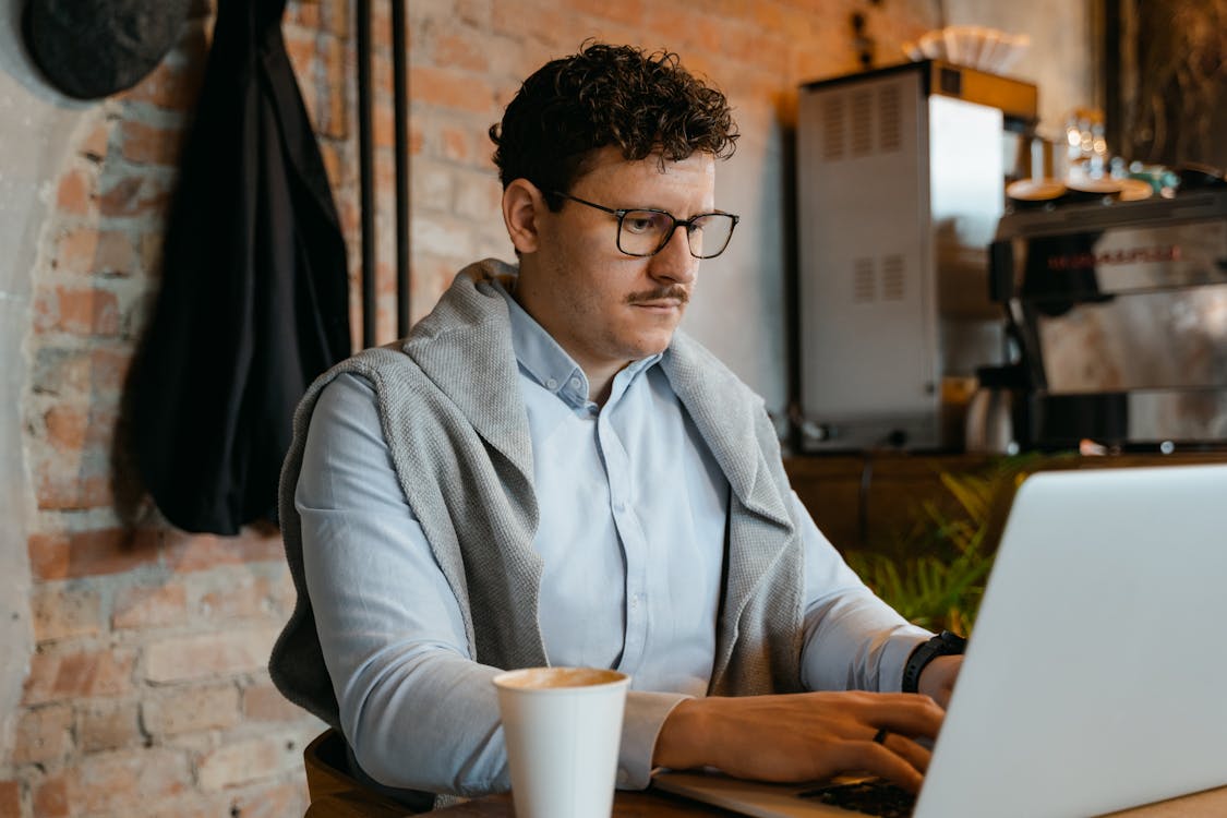 Free A Coffee Cup beside a Man Typing on Laptop Stock Photo