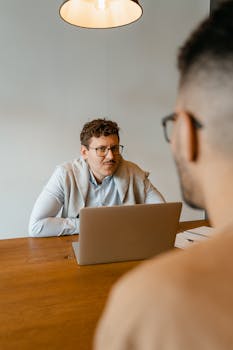Two men engaged in a business meeting at a modern office table with a laptop.