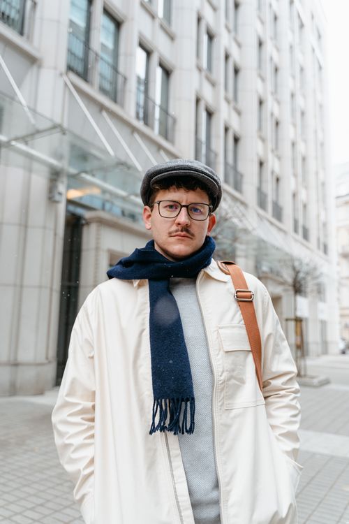 Free Man wearing eyeglasses and a cap standing in front of a building on a city street. Stock Photo