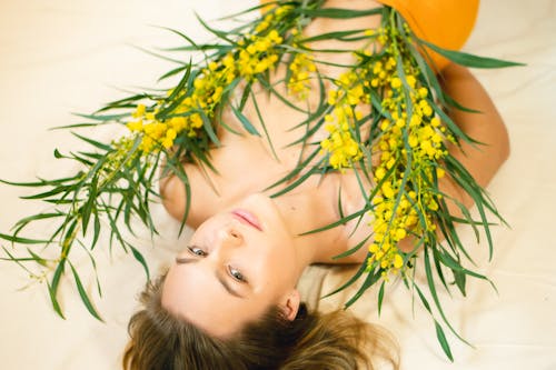 
A Topless Woman Lying Down Covered with Acacia Flowers