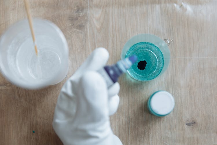 
A Person Pouring Ink In A Container With Resin