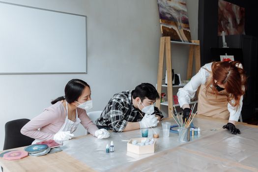 People engaging in a resin art workshop wearing masks and gloves, emphasizing safety and creativity.