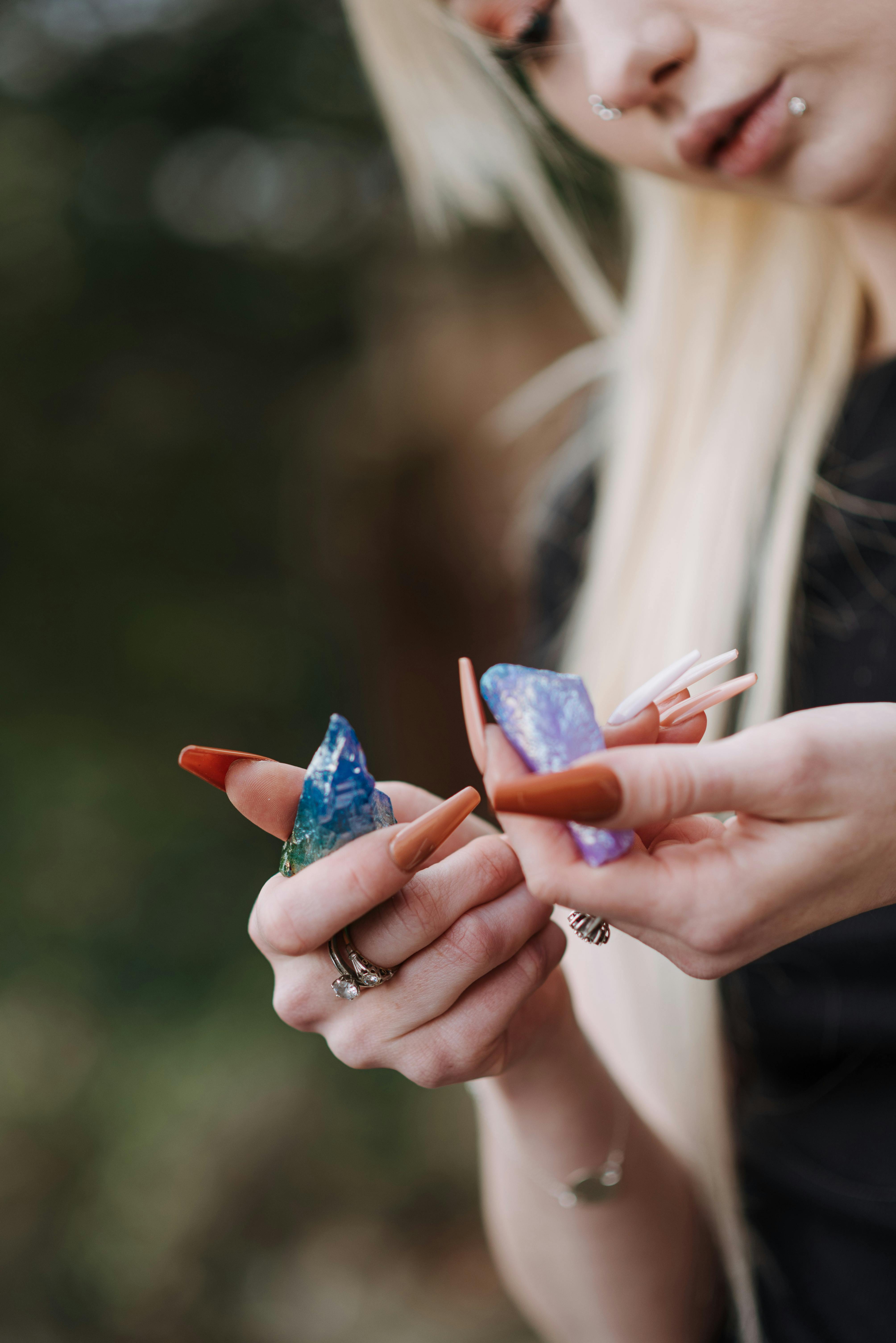 Woman with manicured hands examining bright uncut raw opal stones in natural light, close-up