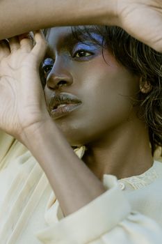 Close-up portrait of a woman with vibrant eye makeup, arms raised, creating an artistic frame.