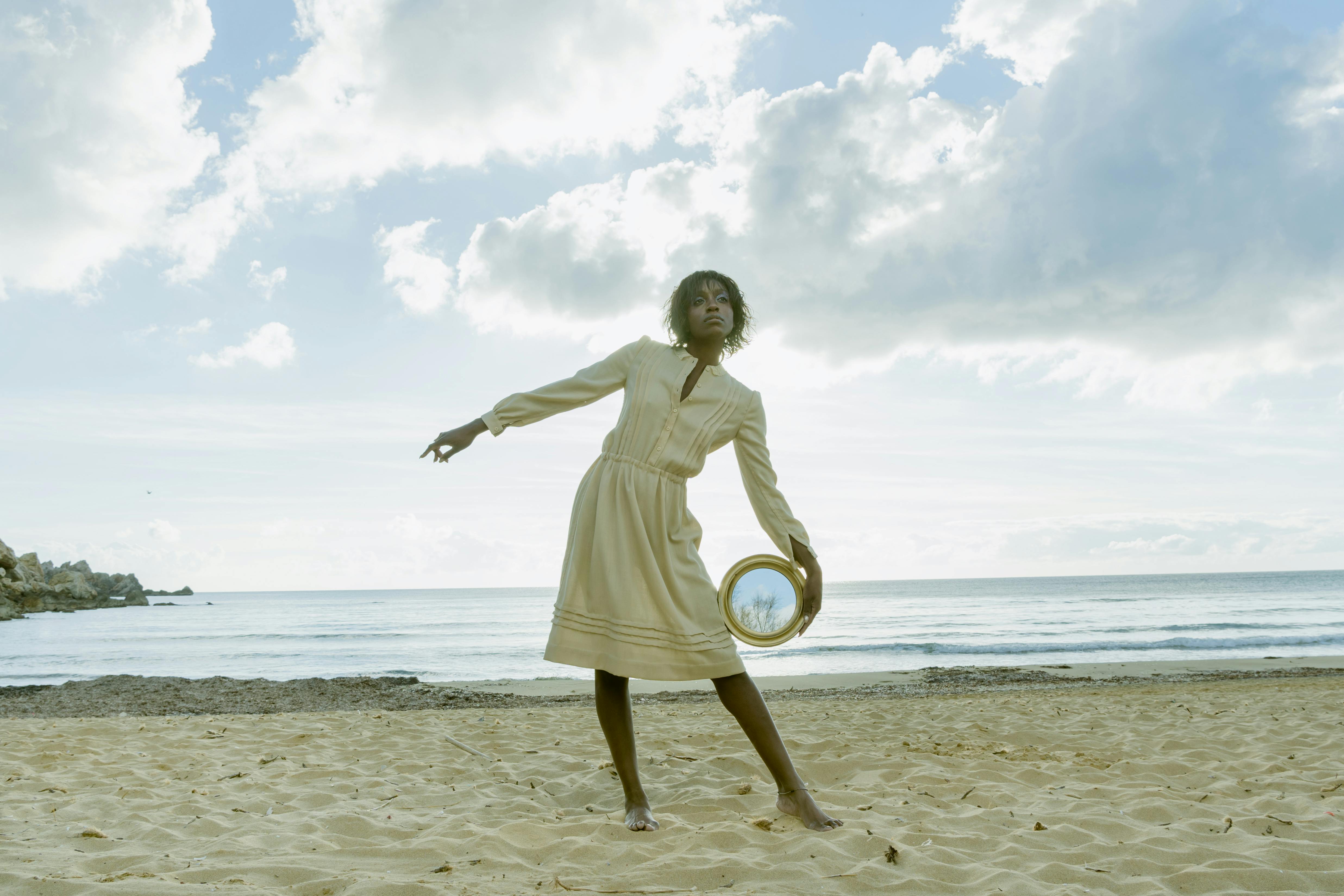 a woman posing in the beach holding a round mirror