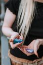 Unrecognizable female with manicured hands standing near meta; railing with bright uncut opals in hands on blurred background on street