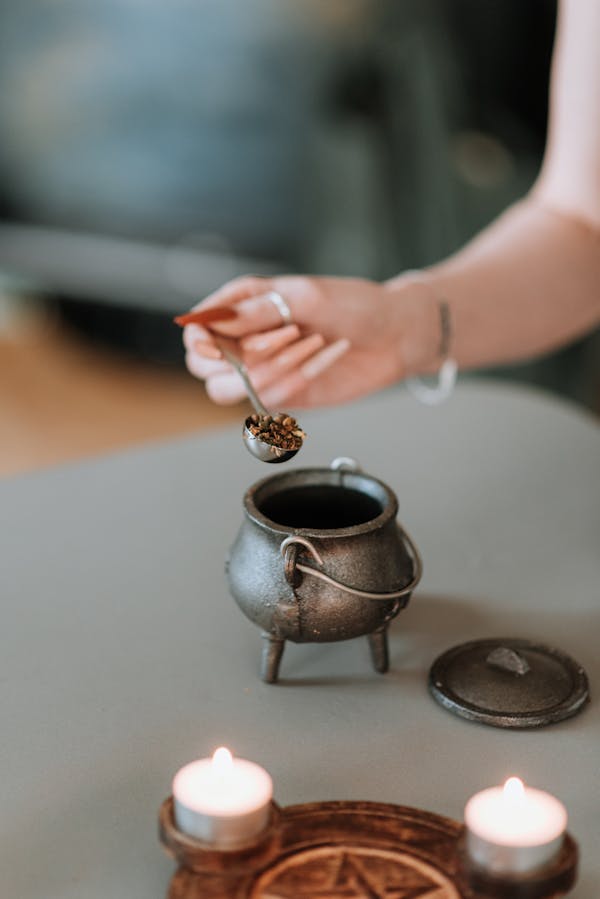 Crop anonymous female adding aromatic spices in incense burner on table with sparkling candles