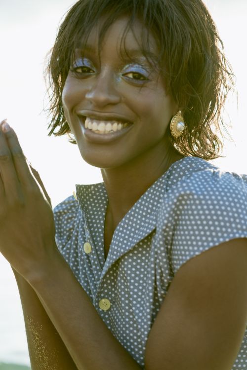 Free A cheerful woman with vibrant blue eyeshadow and a polka dot dress smiles brightly outdoors. Stock Photo