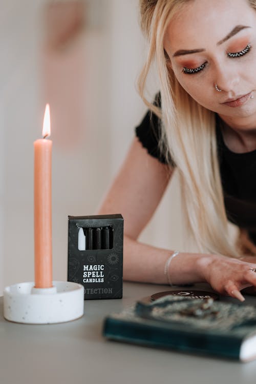 Crop young thoughtful witch at table with box of magic spell candles on blurred background