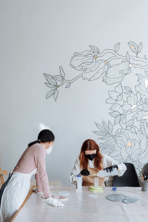 Free Two women wearing masks collaborate on a creative project at a table in a bright studio. Stock Photo