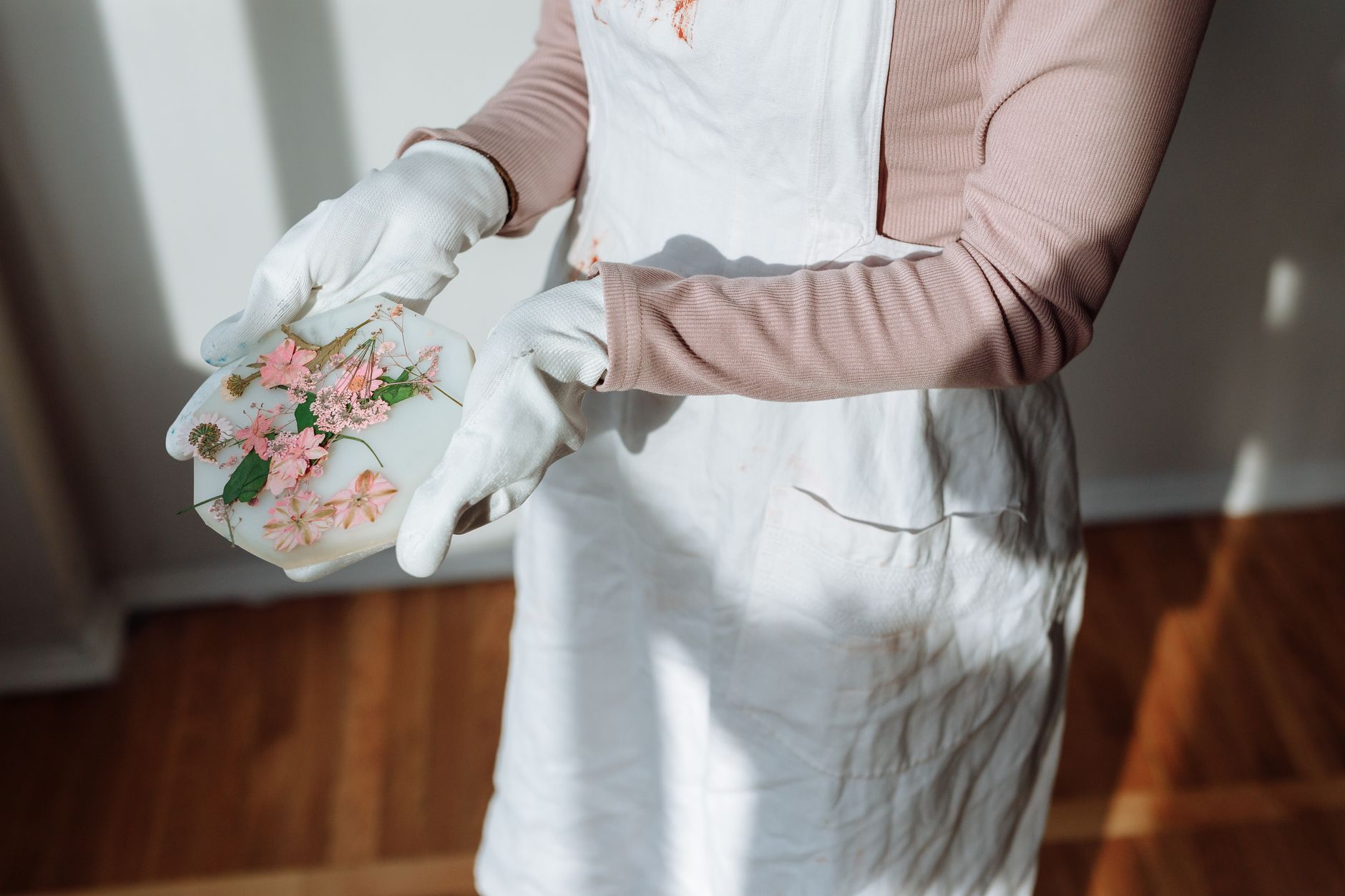 Hands wearing gloves hold a floral resin craft piece on a sunny day indoors.
