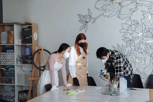 Free Three people engaged in an art workshop, wearing face masks and aprons, fostering creativity. Stock Photo