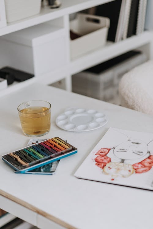 Set of colored crayons near glass with water placed on table with creative drawing and palette in modern light art studio