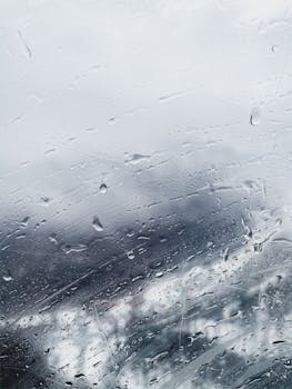 Close-up of rain droplets on glass with a blurred wintery backdrop, capturing the essence of a cold and wet day.