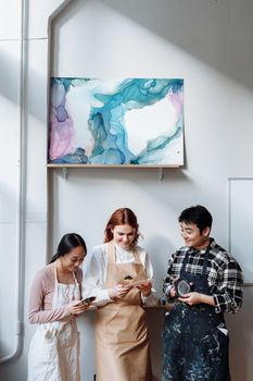 Three artists in aprons discussing art beneath a colorful abstract painting in a studio.