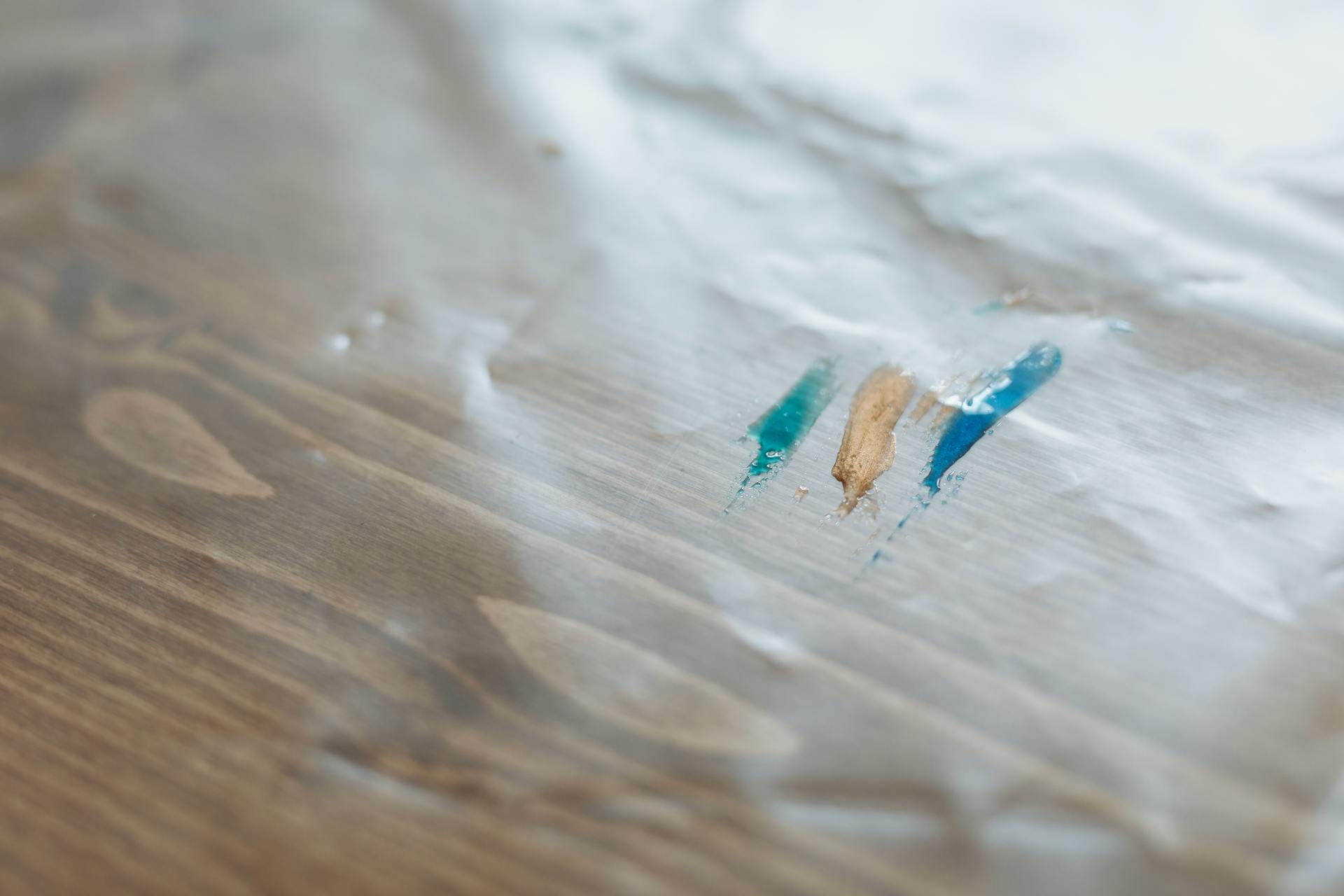 Detailed view of colorful paint streaks on a wooden surface covered in plastic.
