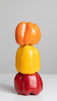Three colorful bell peppers stacked vertically creating a vibrant contrast against a gray background.