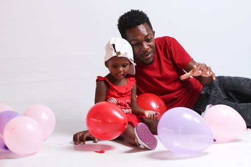 Free A Man in Red Shirt Playing Balloons with Her Daughter in Red Dress Stock Photo
