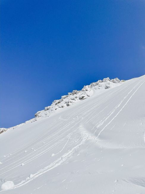 Pristine snowy mountain slope with ski tracks under a vibrant blue sky, capturing winter's serenity.