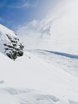 Pristine snow-covered mountain slope under a bright blue sky with fluffy clouds.