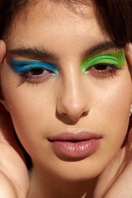 Close-up portrait of a woman with vibrant green and blue eyeshadow and soft pink lips.