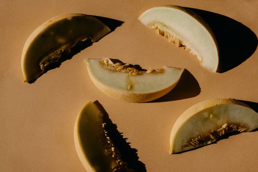 Minimalist still life of honeydew melon slices casting shadows on a brown surface.