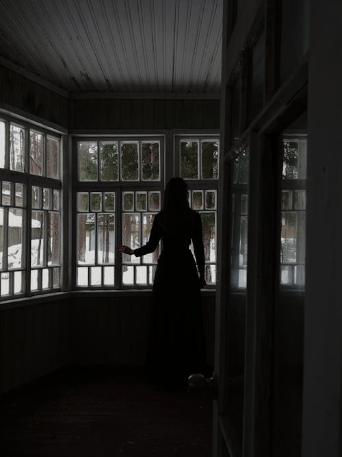 Pensive female standing and looking at window in dark room
